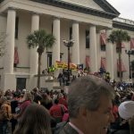 Large crowd of people outside big building with tall pillars