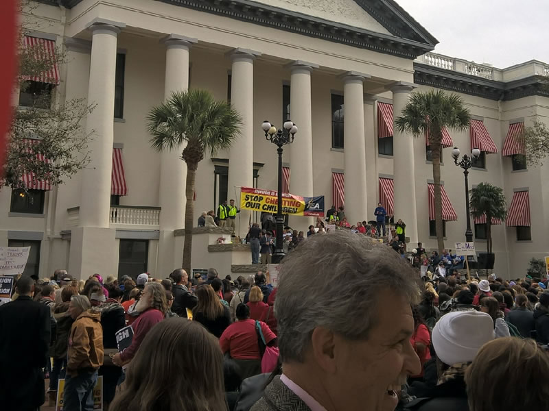 Large crowd of people outside big building with tall pillars